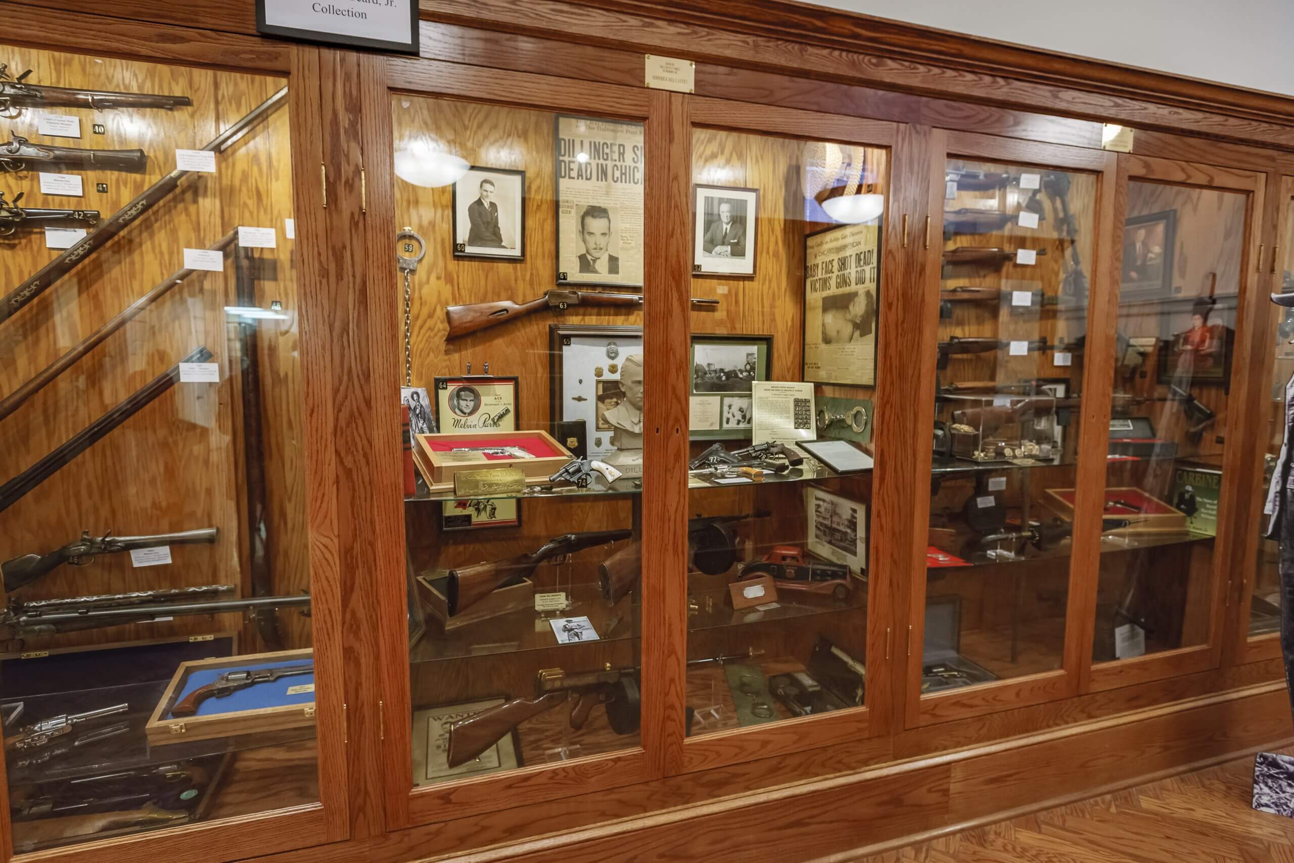 camdenarchivesmuseum-exhibit4 Wooden museum display case stocked with antique rifles, photos, and vintage memorabilia inside glass panels.
