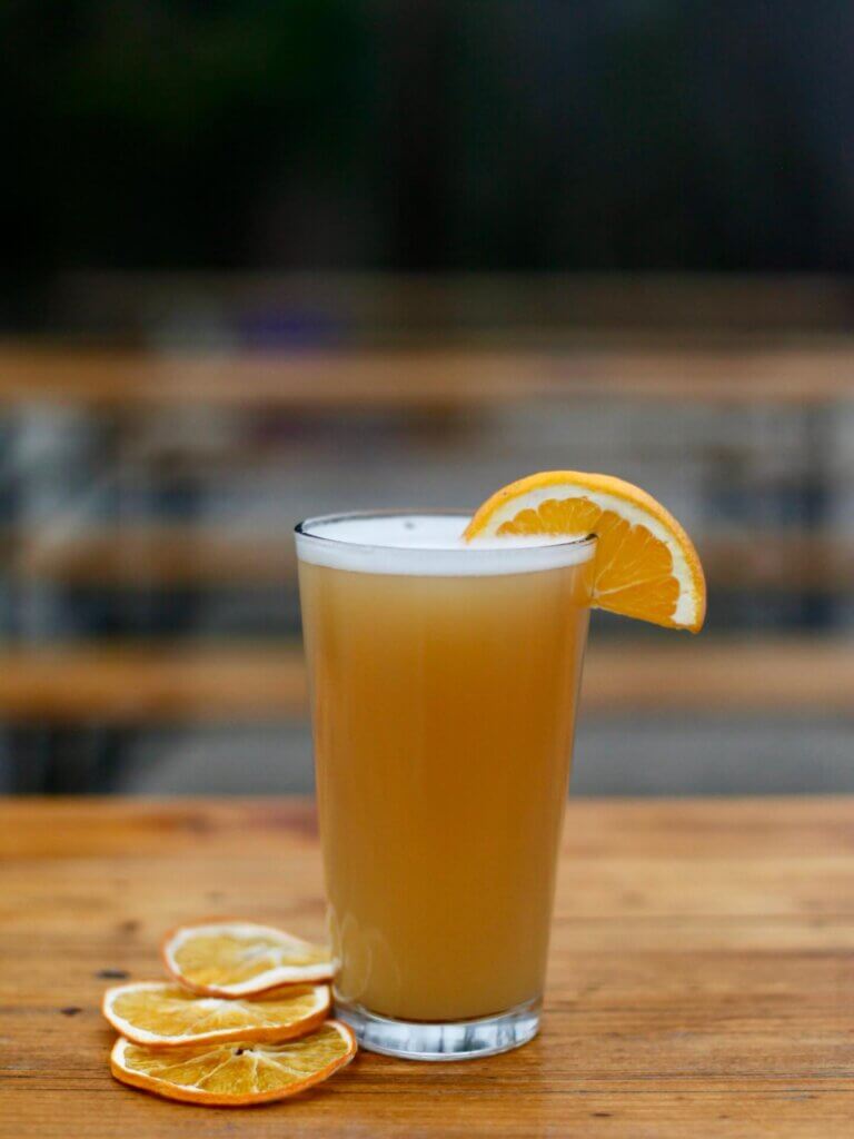 GP beer - Experience Camden, South Carolina A tall glass of orange juice with a slice of orange on the rim, on a wooden table with dried orange slices nearby.