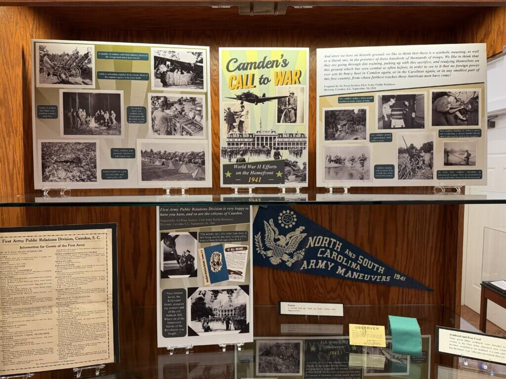IMG_4897 - Experience Camden, South Carolina Historical museum display: a collage of black-and-white WWII posters and photos mounted on a wood panel shelf, including a prominent 'Camden's Call to War' panel.