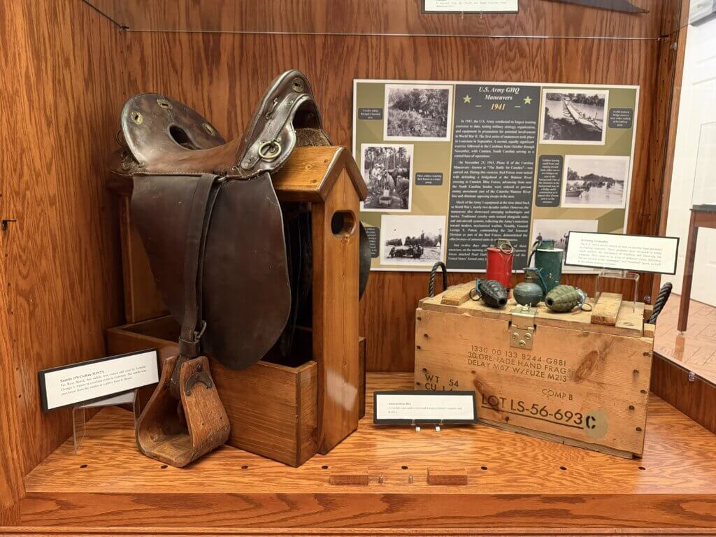 IMG_4898 - Experience Camden, South Carolina Historical museum display of a large leather riding saddle on a wooden stand beside an information board with black-and-white photos and text panels.