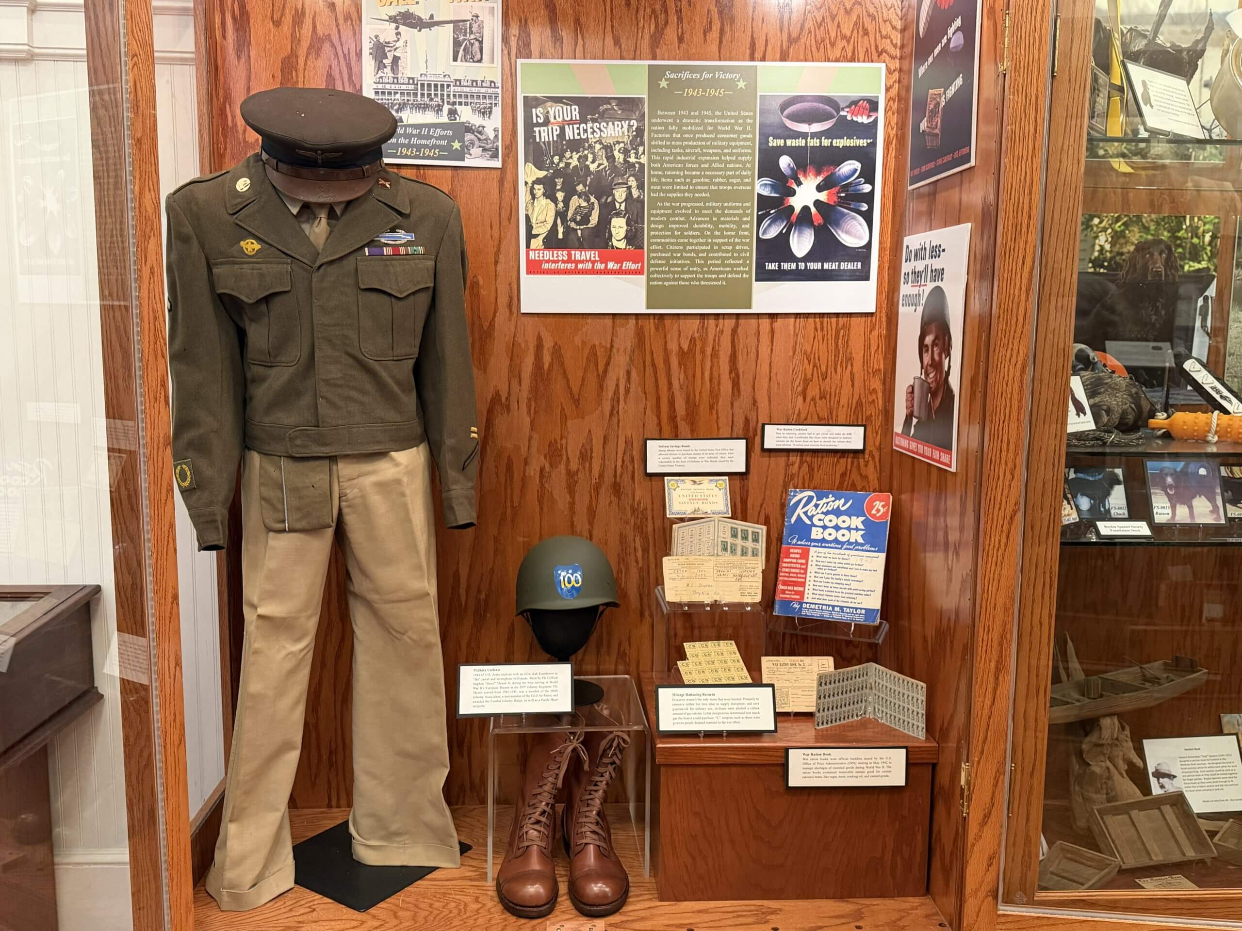 IMG_4909 Military uniform on a mannequin with a peaked cap and ribbons, displayed beside WWII-era posters on a wood-paneled wall.
