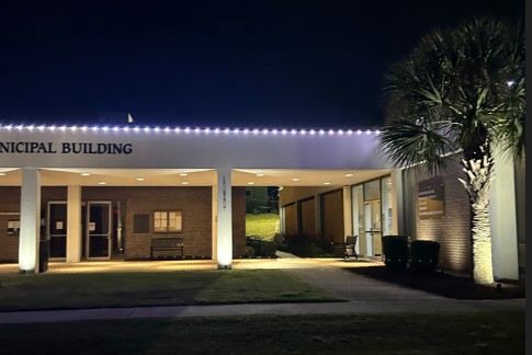 Screenshot 2026-05-01 111528 Nighttime exterior of a municipal building with a lit entrance, a palm tree, and string lights along the roof edge.