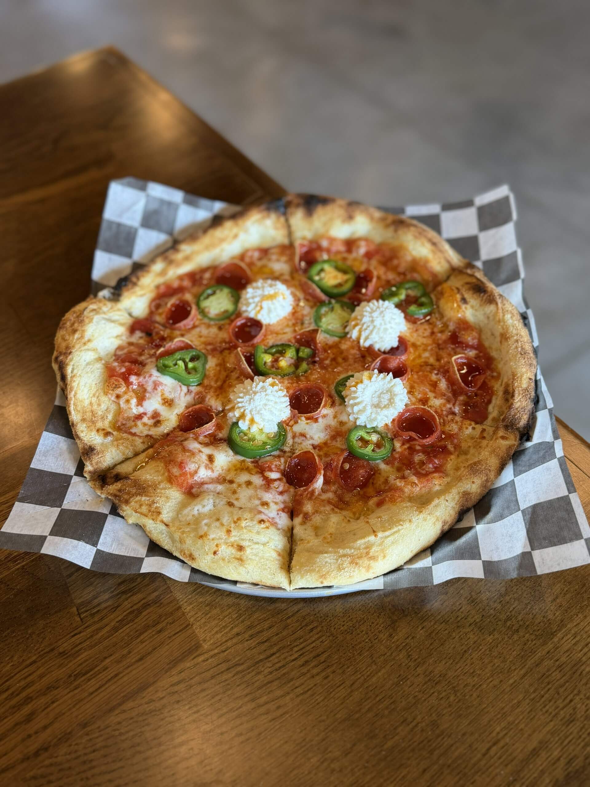 pizza - Experience Camden, South Carolina Large round pizza with pepperoni, jalapeño slices, and dollops of ricotta on a crispy crust, placed on checkered parchment.