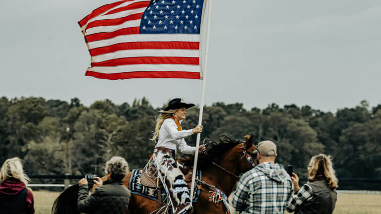 hero6-768×432 horse and hound Camden girl riding a horse holding the United States of America flag