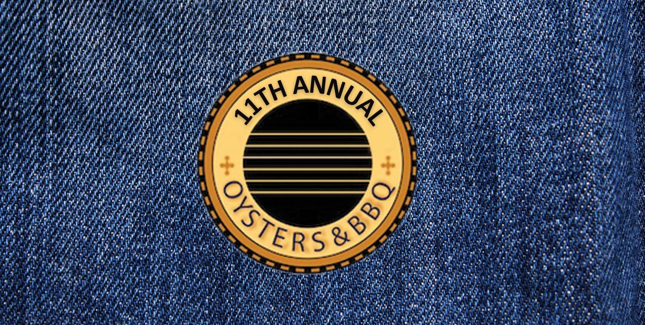 2026 Header (1).jpg - Experience Camden, South Carolina A round gold pin reading 11th Annual Oysters & BBQ lies on blue denim fabric.