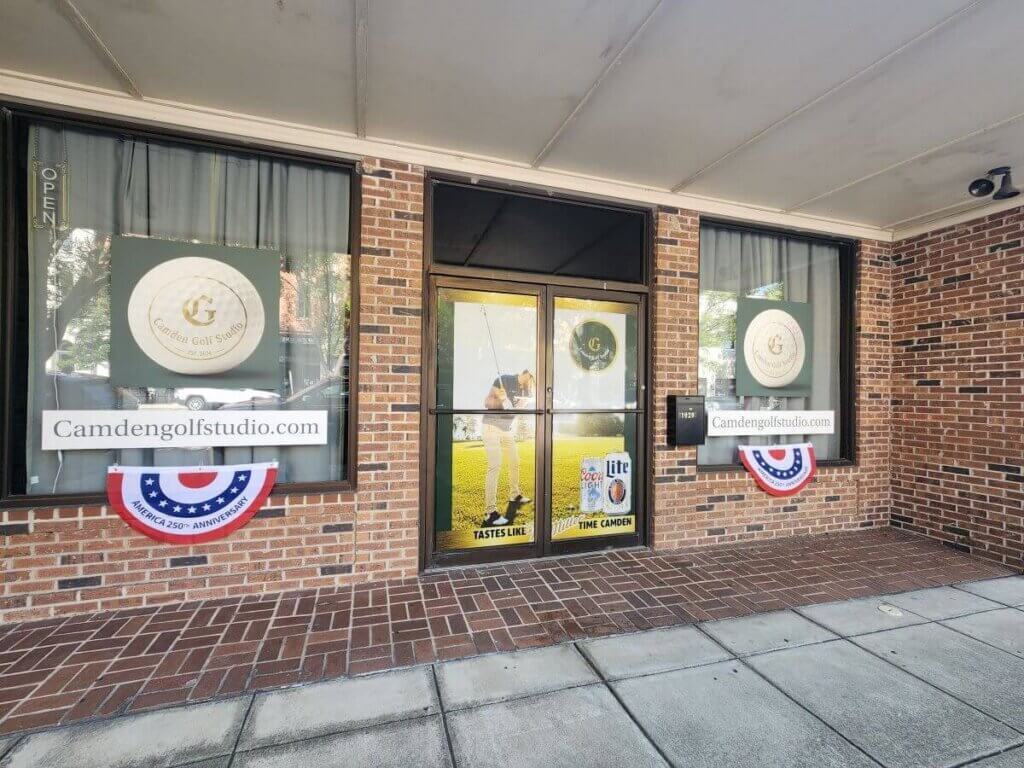 camden golf studio - Experience Camden, South Carolina Storefront of Camden Golf Studio with large logos on the windows, a gold golfer graphic on the door, two patriotic bunting banners, and a website URL, camdengolfstudio.com, displayed.