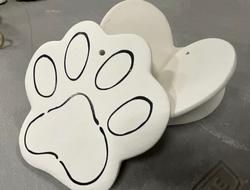 IMG_3495.jpeg - Experience Camden, South Carolina Two white paw-shaped ceramic pieces, one with a black outlined paw print and one plain, both resting on a gray surface.