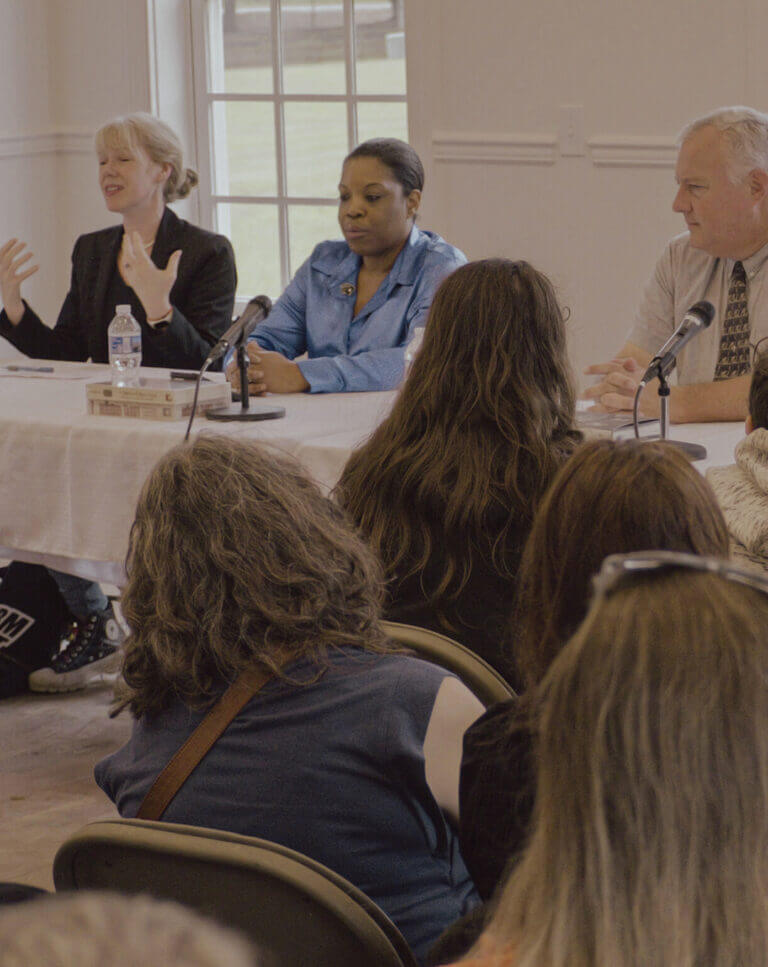 Voodoo Panel Southern Gothic 2025 - Experience Camden, South Carolina Three people sit at a table with microphones, speaking to an audience. One woman gestures with her hands, while the others listen. The audience is seated and facing the speakers in a well-lit room with large windows.
