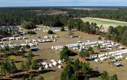 CRWW Overhead View - Experience Camden, South Carolina Aerial view of a sprawling encampment with rows of white tents situated in a clearing surrounded by a pine forest.