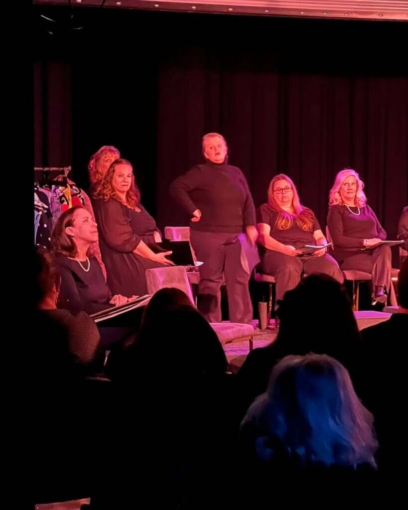 arts center 2025 - Experience Camden, South Carolina A group of women in black clothing on the Black Box stage, with one woman standing and the others seated with scripts in their laps.