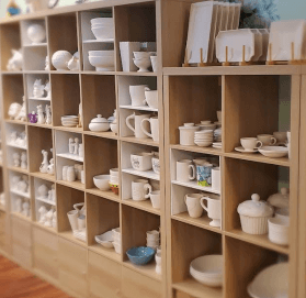 dodonjeans - Experience Camden, South Carolina Wooden shelving unit filled with assorted white ceramic bowls, mugs, plates, and decorative figurines.