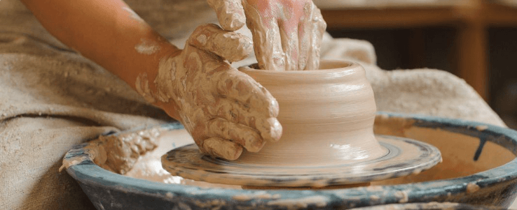 pottery class - Experience Camden, South Carolina Hands covered in clay shaping a vessel on a pottery wheel.